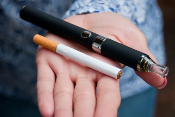 一個人的掌心中同時放著一支傳統紙菸與一支黑色電子菸主機,背景模糊,呈現出兩種不同煙草與尼古丁產品的視覺對比。
