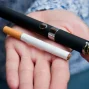 一個人的掌心中同時放著一支傳統紙菸與一支黑色電子菸主機，背景模糊，呈現出兩種不同煙草與尼古丁產品的視覺對比。