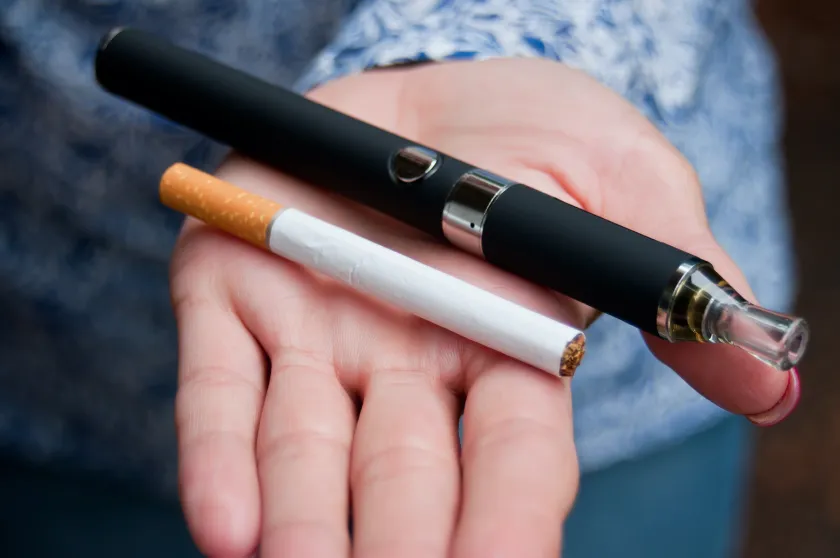 一個人的掌心中同時放著一支傳統紙菸與一支黑色電子菸主機,背景模糊,呈現出兩種不同煙草與尼古丁產品的視覺對比。